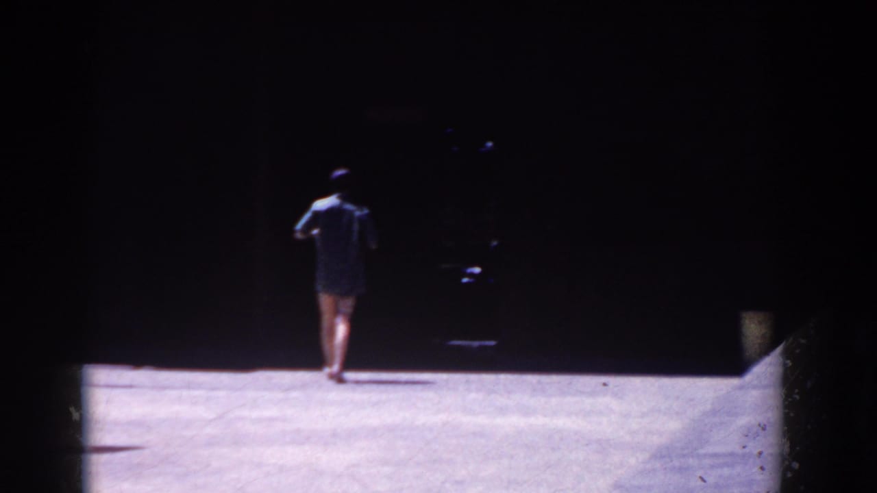 A person in dark swimwear walks away across a bright open surface toward deep shade.