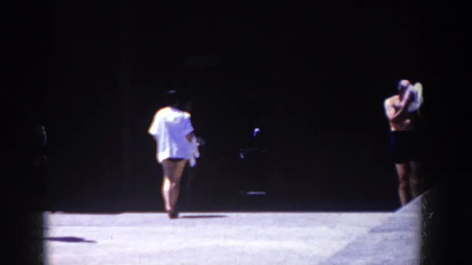 A man in a white shirt walks away in the 1958 French Lick scene as another bather stands near the dark edge of the frame.
