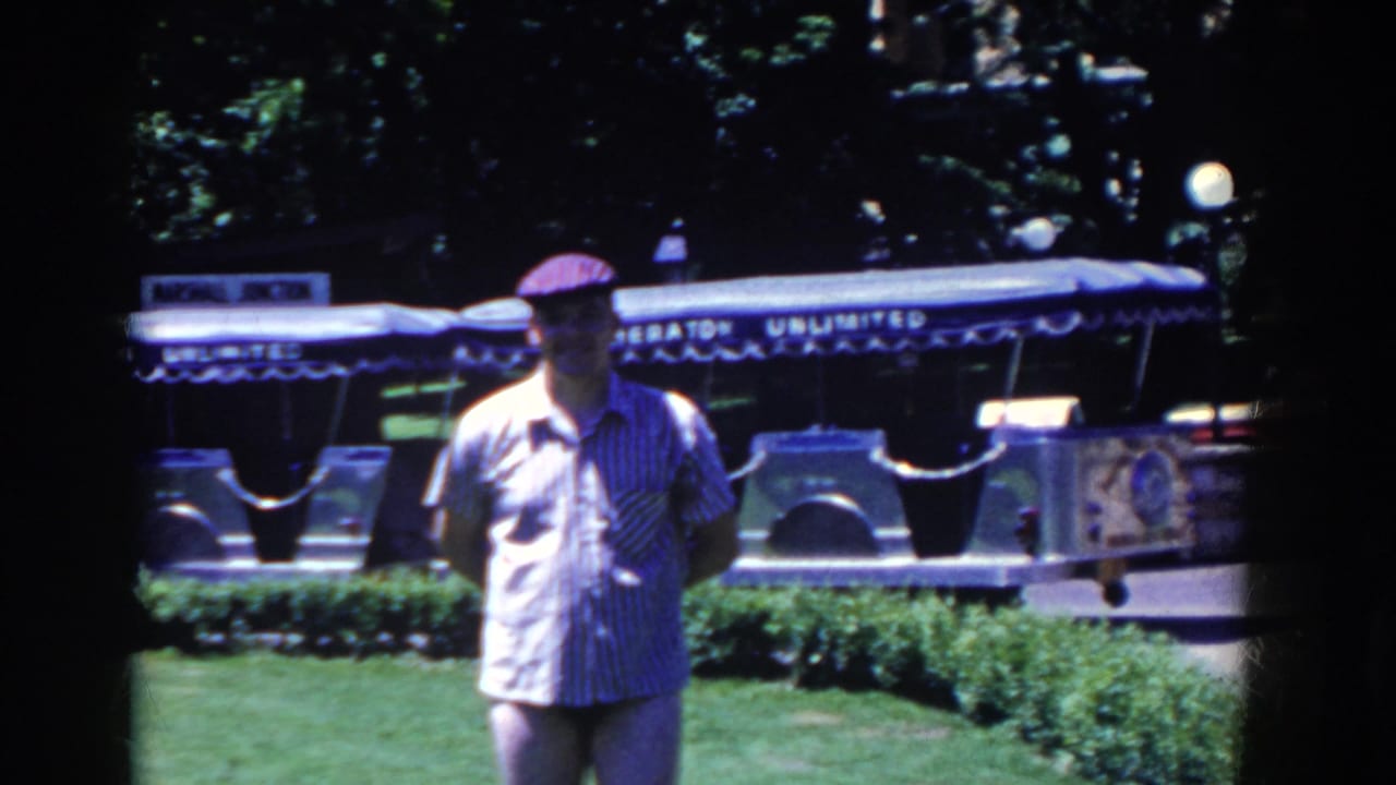 Man in a cap stands on grass in front of a tour tram with lettering.