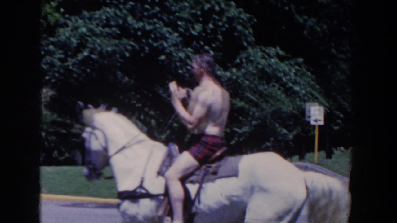 In 1958 French Lick, Indiana, a shirtless man in plaid shorts rides a white horse on a tree-lined paved road.