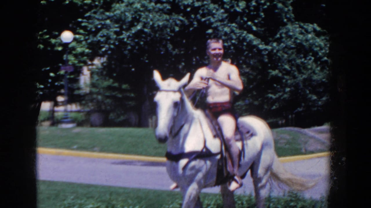 In 1958 French Lick, Indiana, a shirtless man rides a white horse toward the camera along a grassy park path.