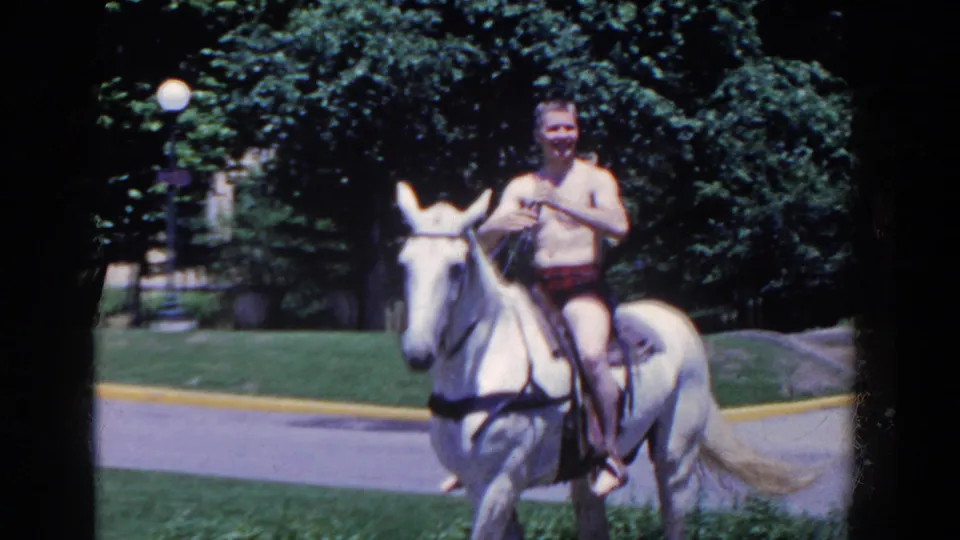 In 1958 French Lick, Indiana, a shirtless man rides a white horse toward the camera along a grassy park path.