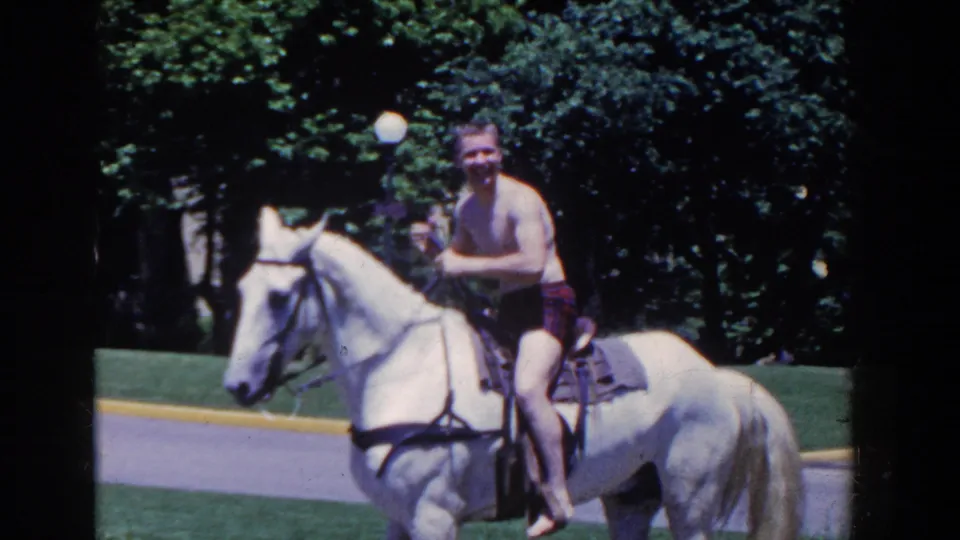 The rider looks toward the camera while seated on a white horse in the French Lick park setting.
