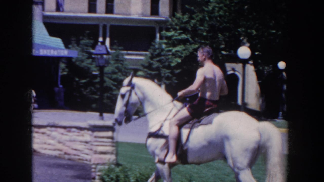 In French Lick, Indiana, a shirtless man rides a white horse near the hotel facade, trees, lawn, and green awning in 1958 home-movie footage.