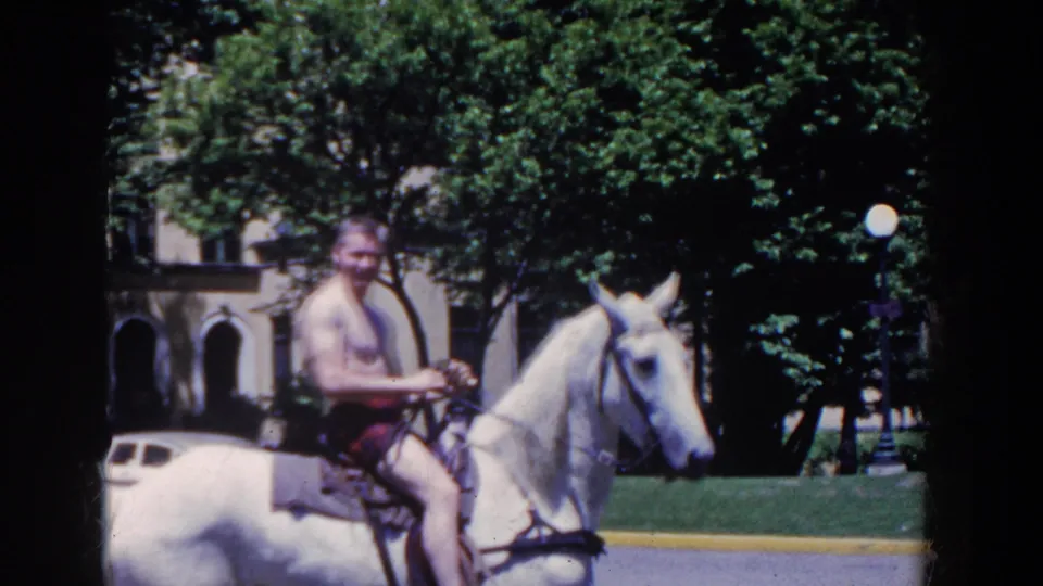 The rider continues past trees and arched hotel architecture on a white horse during the 1958 French Lick, Indiana home-movie scene.