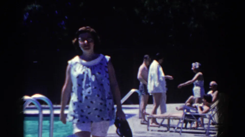 A close poolside frame shows the woman passing near the lens, with French Lick resort guests, ladder rails, chairs, and pool water visible behind her.