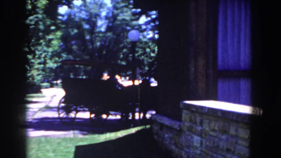 Near the end of the shot, the buggy moves away along the street beside a stone wall, with a shaded window or curtain at the right edge.