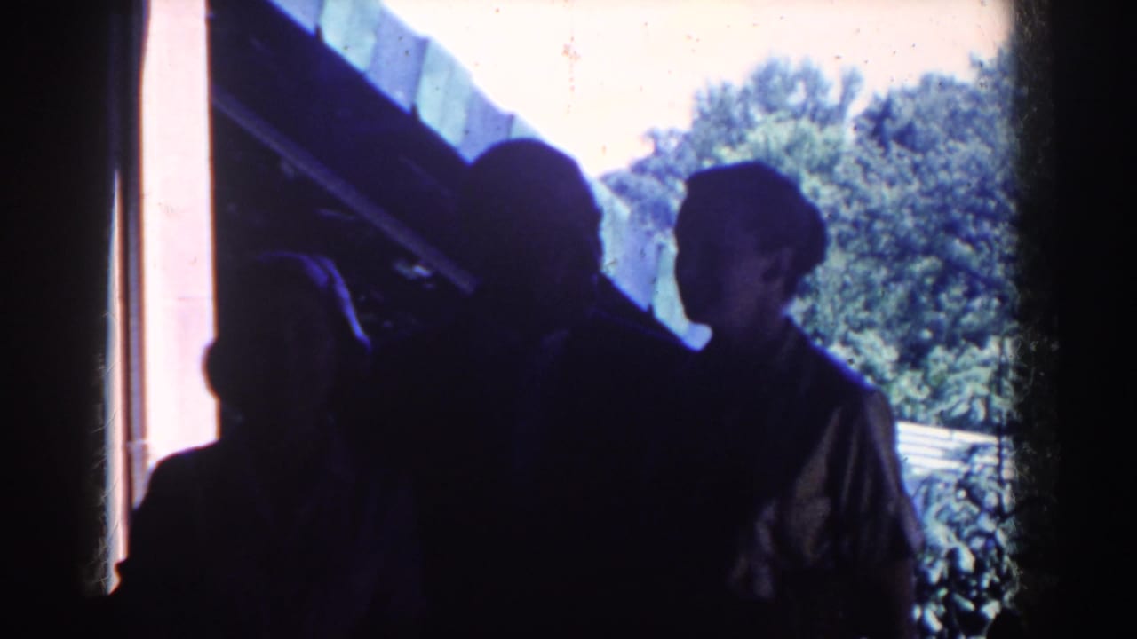 Three silhouetted adults stand near a doorway with trees and a roofline outside.