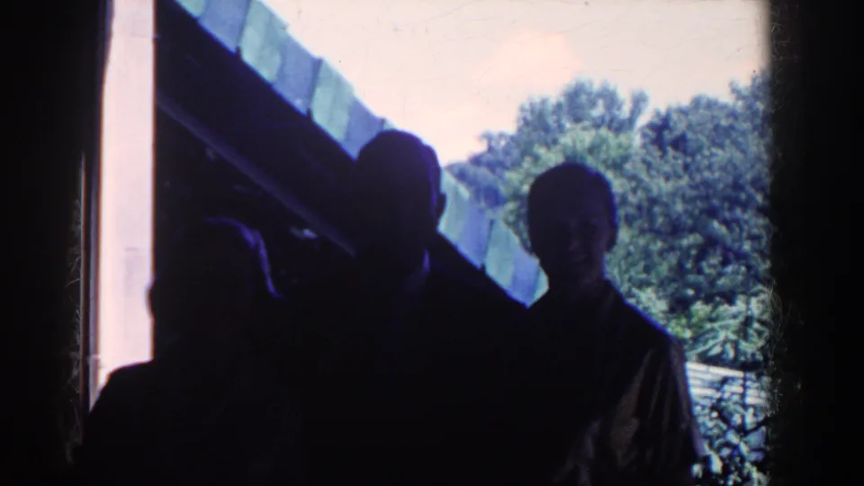Near the end of the clip, a woman turns toward the camera beside two silhouetted adults at the French Lick house entrance.