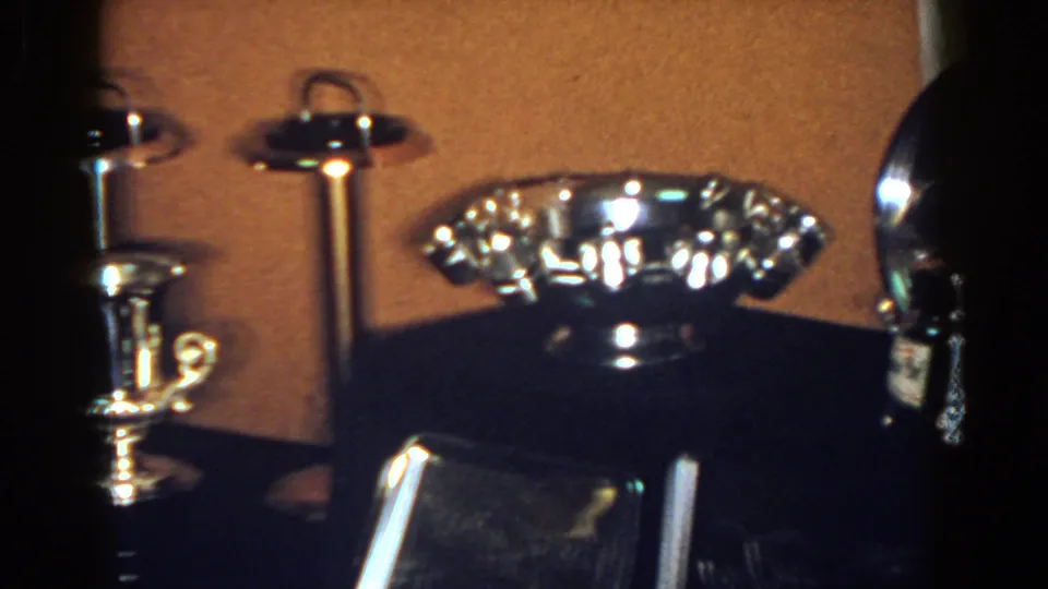 1958 French Lick frame showing a fluted silver-toned bowl, trophy-style cup, pedestal ashtrays, and nearby dark objects.