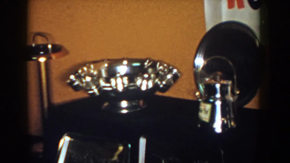 1958 French Lick frame centered on a fluted silver-toned bowl with a dark round object and other reflective pieces nearby.