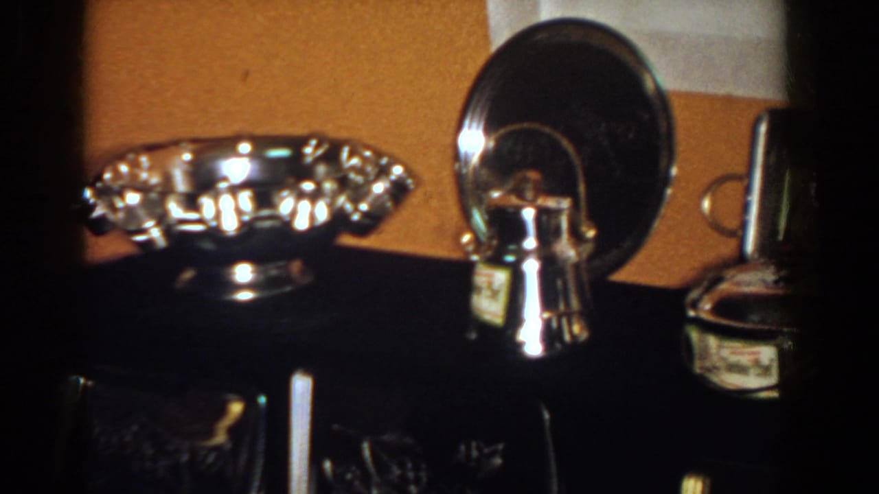 1958 French Lick home-movie frame showing reflective awards and keepsakes on a dark console.
