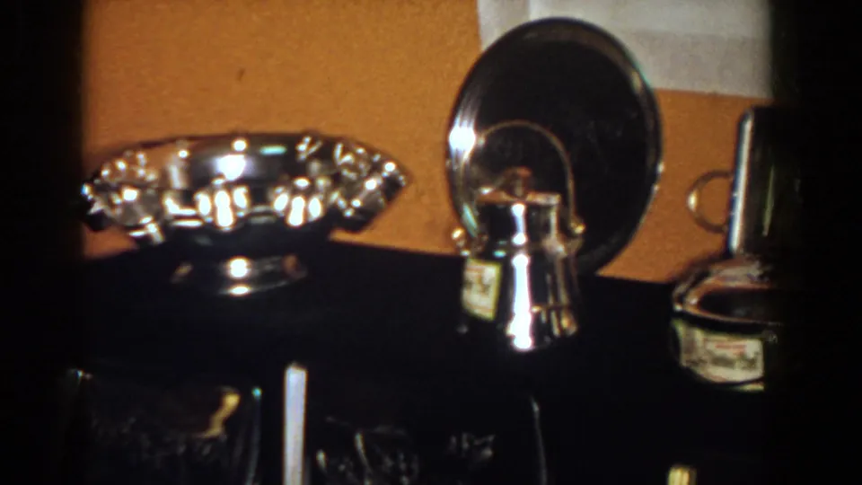 1958 French Lick home-movie frame showing reflective awards and keepsakes on a dark console.