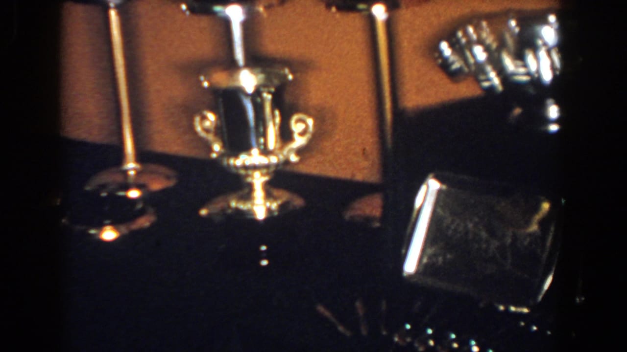 Polished metal cup, candlesticks, and rectangular case on a dark surface.