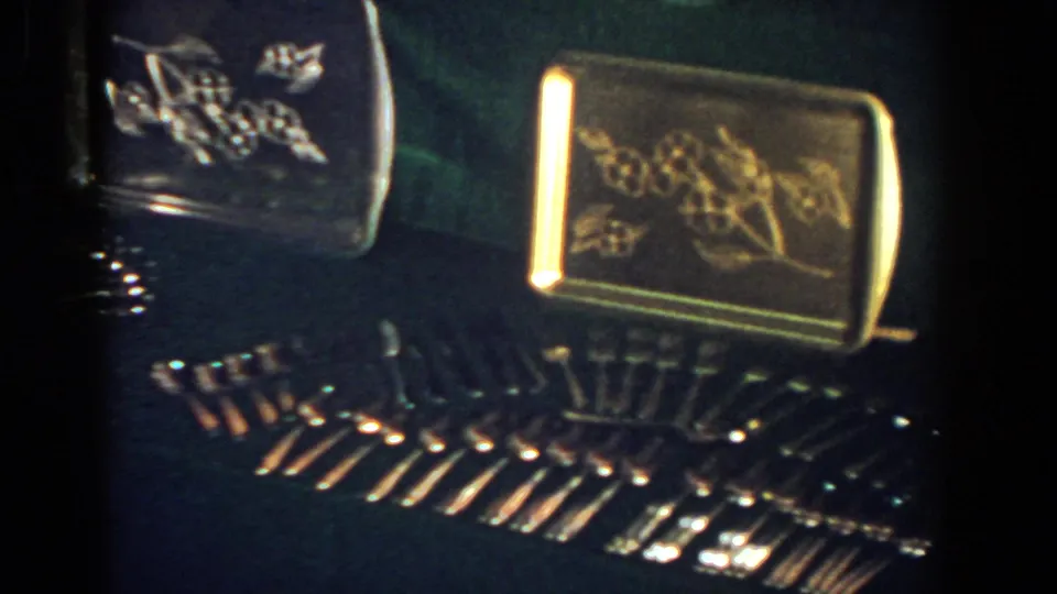1958 French Lick 8mm frame showing gold-toned engraved trays and reflective stemware arranged on a dark tabletop.