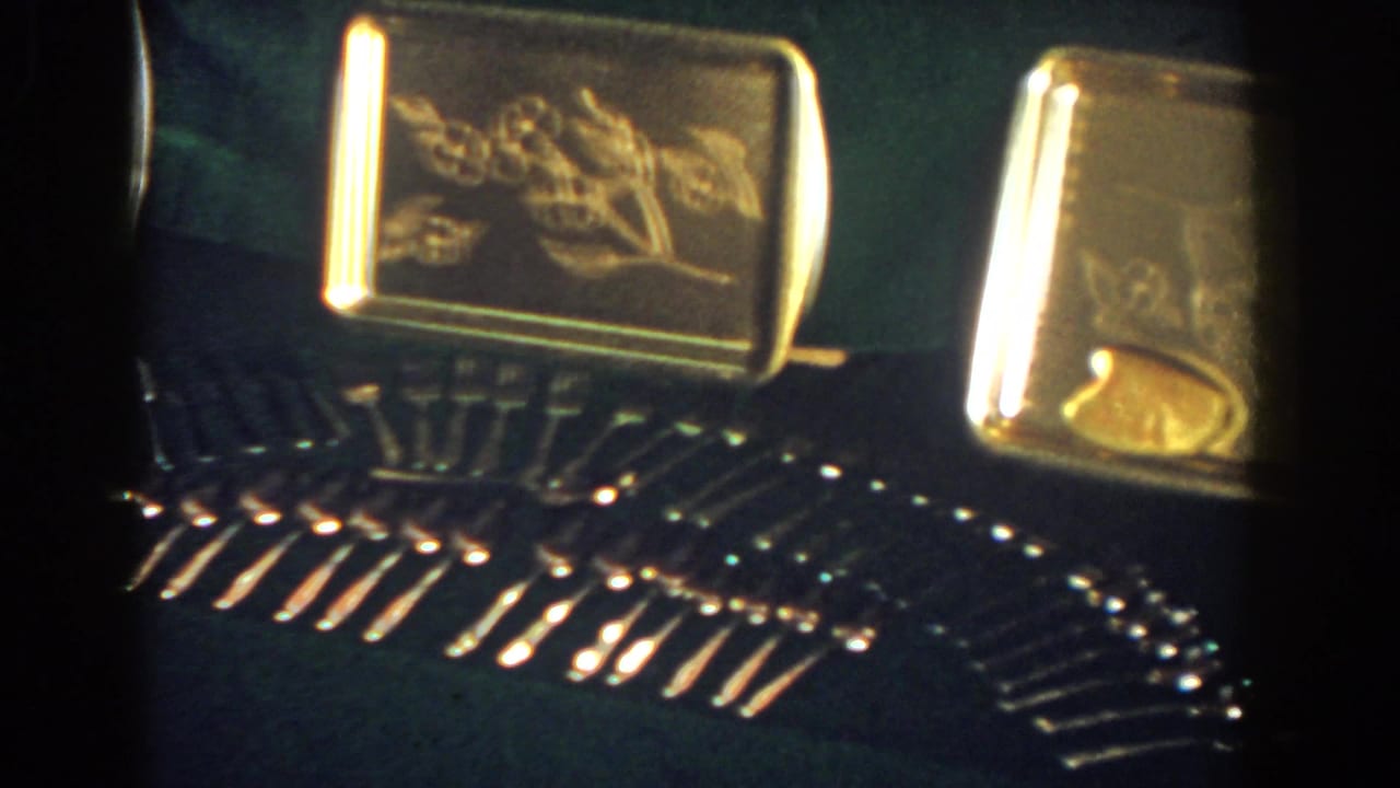 1958 French Lick 8mm frame with engraved gold-toned trays and neatly arranged reflective stemware on a dark surface.