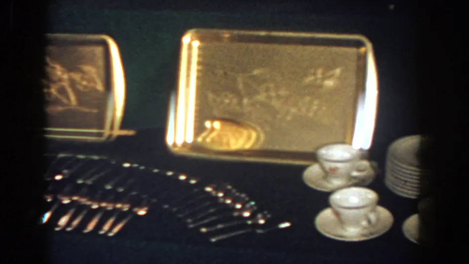 1958 French Lick 8mm frame showing a gold-toned tray with stemware, white teacups, saucers, and stacked plates nearby.