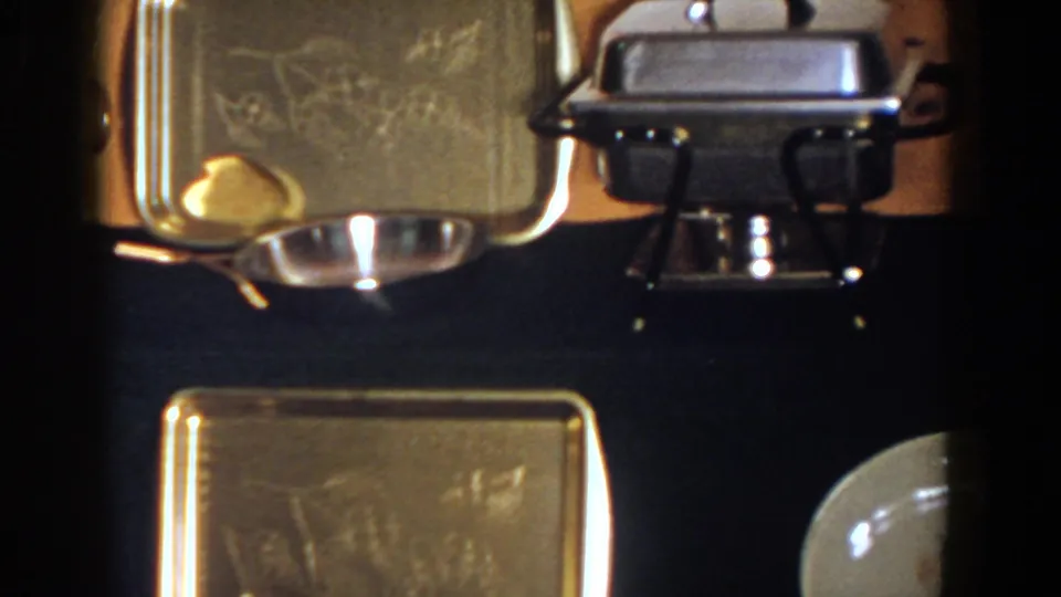 1958 French Lick home-movie frame showing silver trays, a chafing dish, and china on a dark table surface.