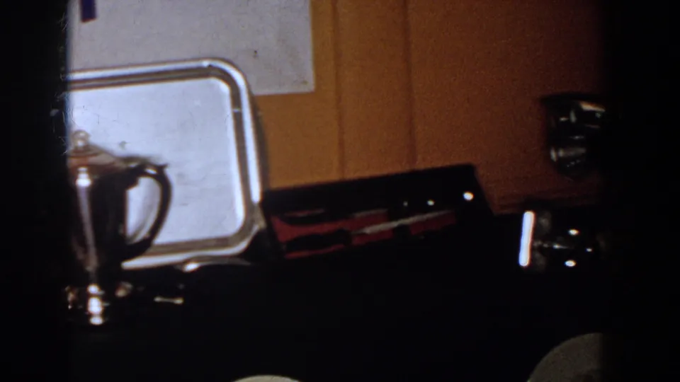 1958 French Lick frame showing a silver teapot and tray on a dark table with wood paneling behind.