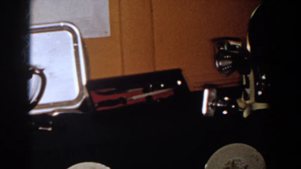 1958 French Lick home-movie frame showing a silver tray and other reflective metal objects on a dark surface.