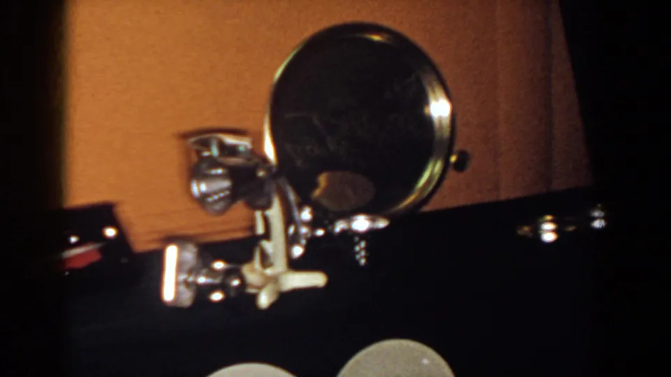 Close 8mm view of a chrome-framed round mirror and small metal object in a dim French Lick interior.