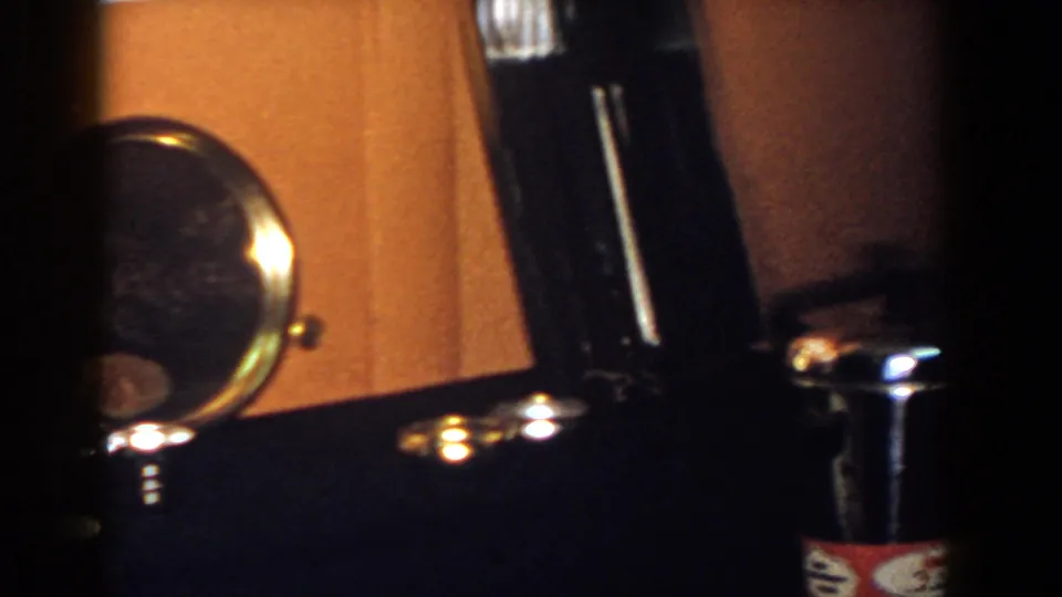 Handheld 1958 frame with a round mirror partly cropped beside shiny metal fittings on a dark tabletop.