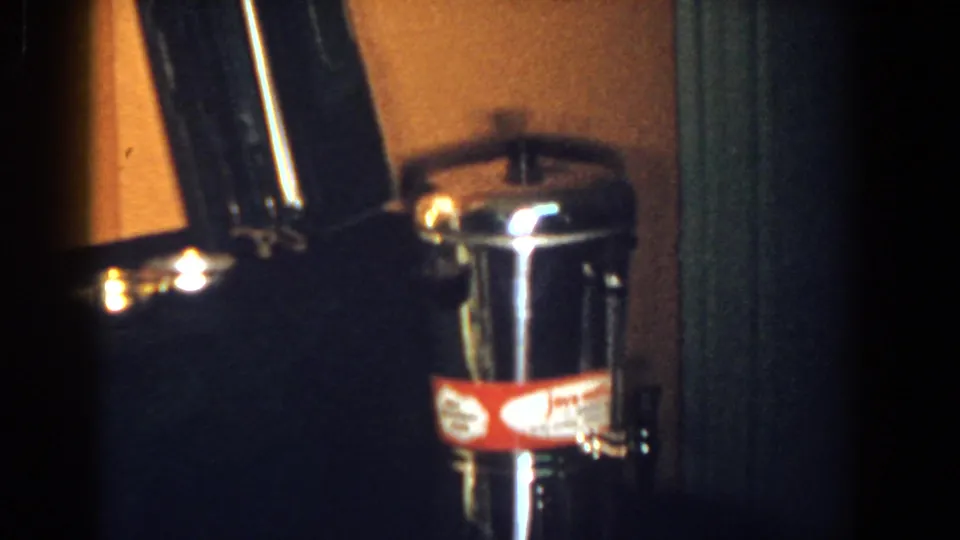 French Lick 1958 home-movie frame showing a shiny cylindrical metal container with a red label on a dark surface.