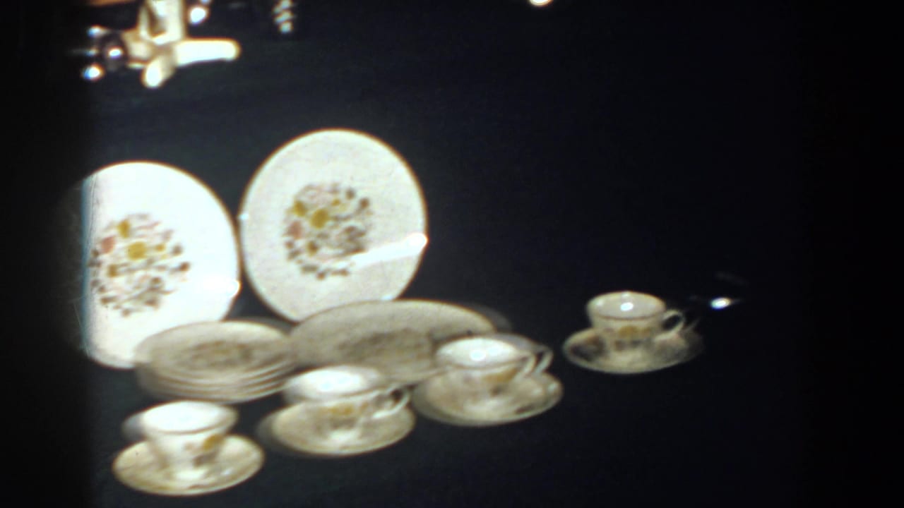 1958 French Lick frame showing white floral dinnerware, stacked saucers, and small cups arranged for display.