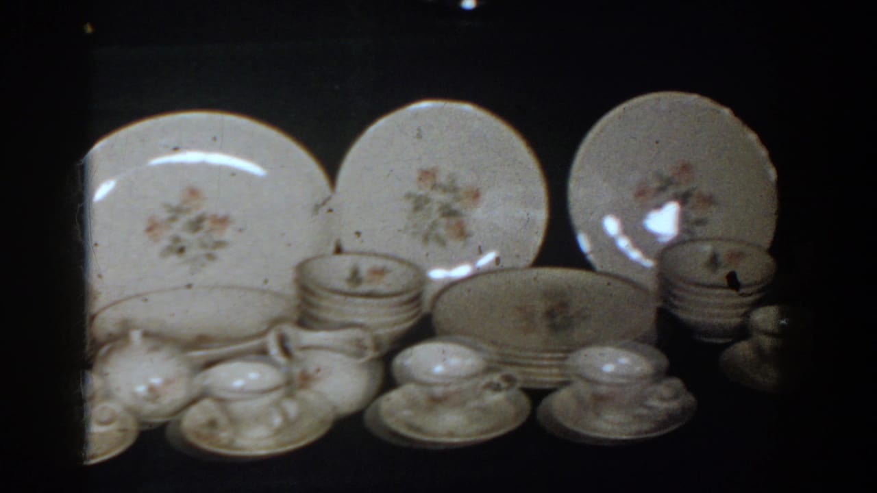 1958 French Lick home-movie frame showing floral porcelain plates, cups, saucers, and serving pieces arranged for display.