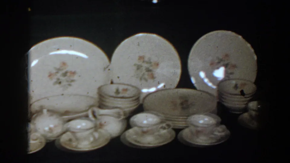1958 French Lick home-movie frame showing floral porcelain plates, cups, saucers, and serving pieces arranged for display.