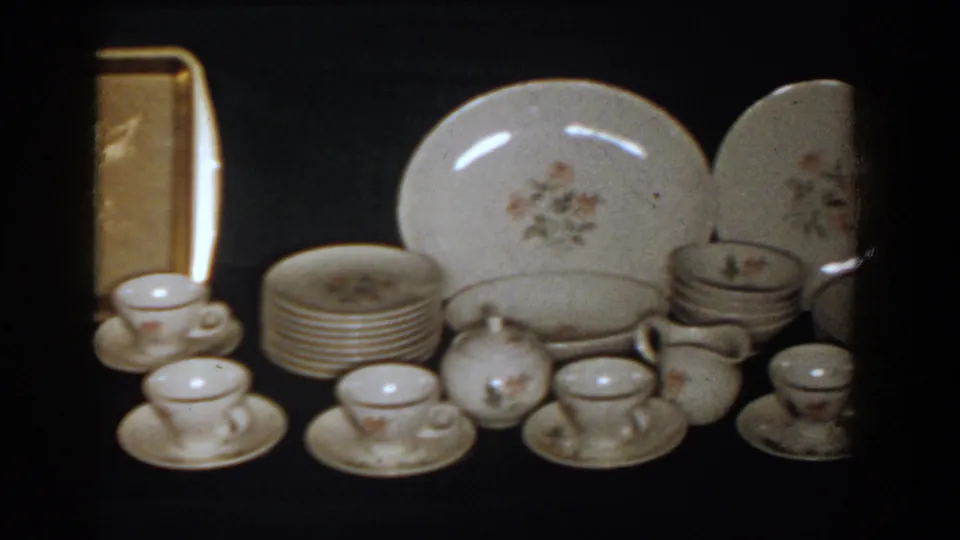 1958 French Lick frame with a porcelain dinnerware set, stacked plates, small serving pieces, and a gold-toned tray behind them.