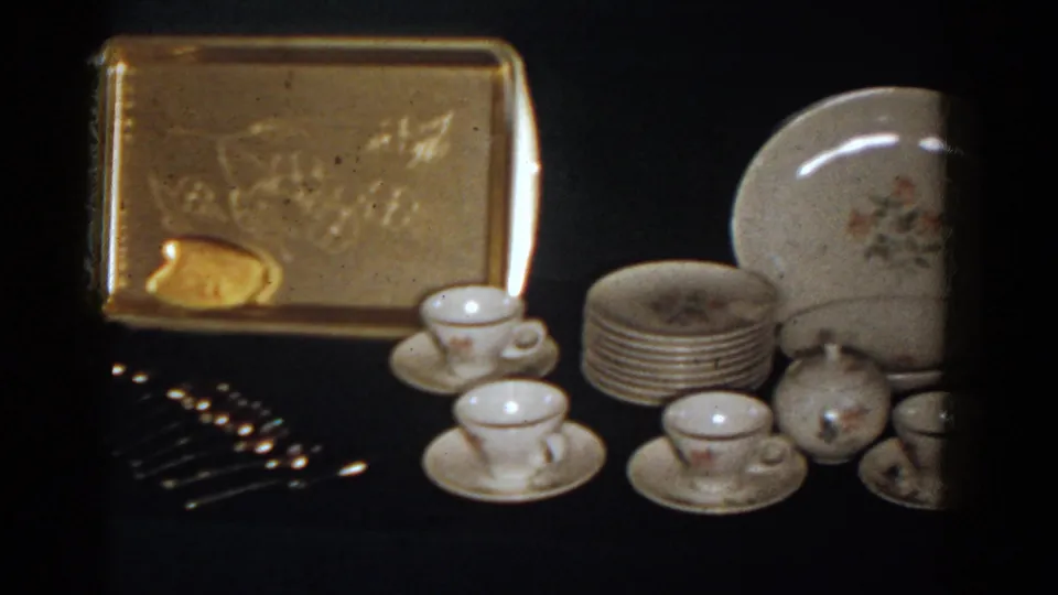 Close display view of a gold-toned tray, silverware, porcelain cups, saucers, and stacked plates from the 1958 French Lick footage.
