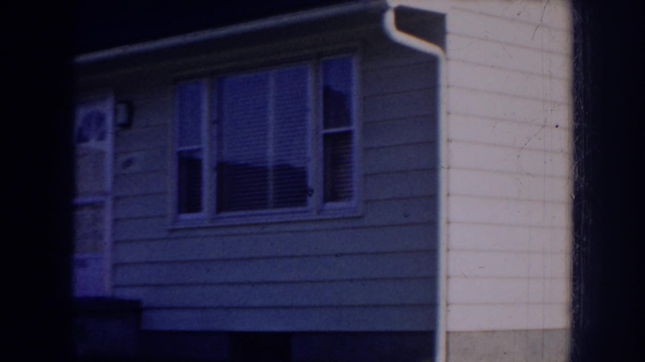 A light-colored suburban house exterior in Nebraska, with front windows, door, siding, porch edge, and deep frame shadow.