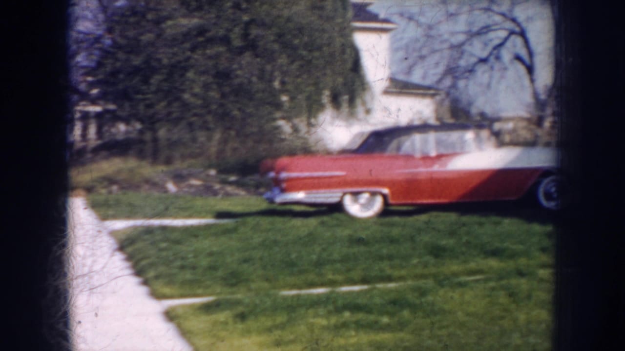 Red-and-white convertible parked on a lawn beside a sidewalk and house.