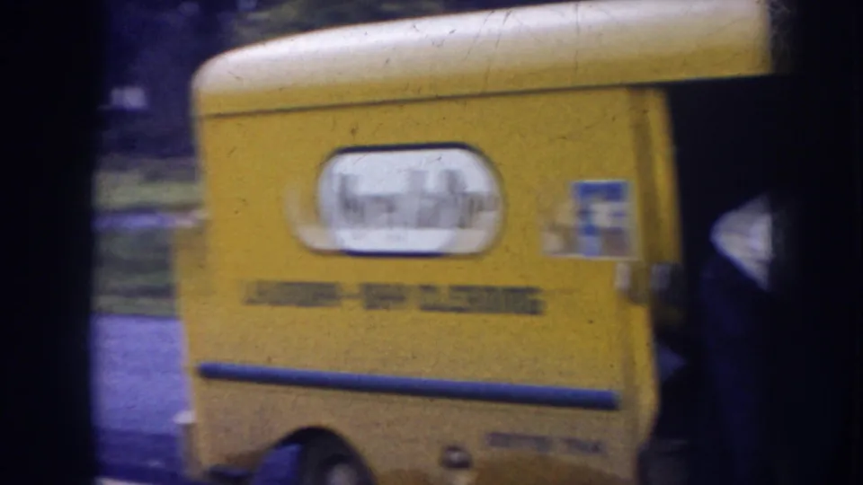 Yellow delivery truck in a Nebraska residential setting, with partial laundry and dry cleaning business lettering visible on its side.