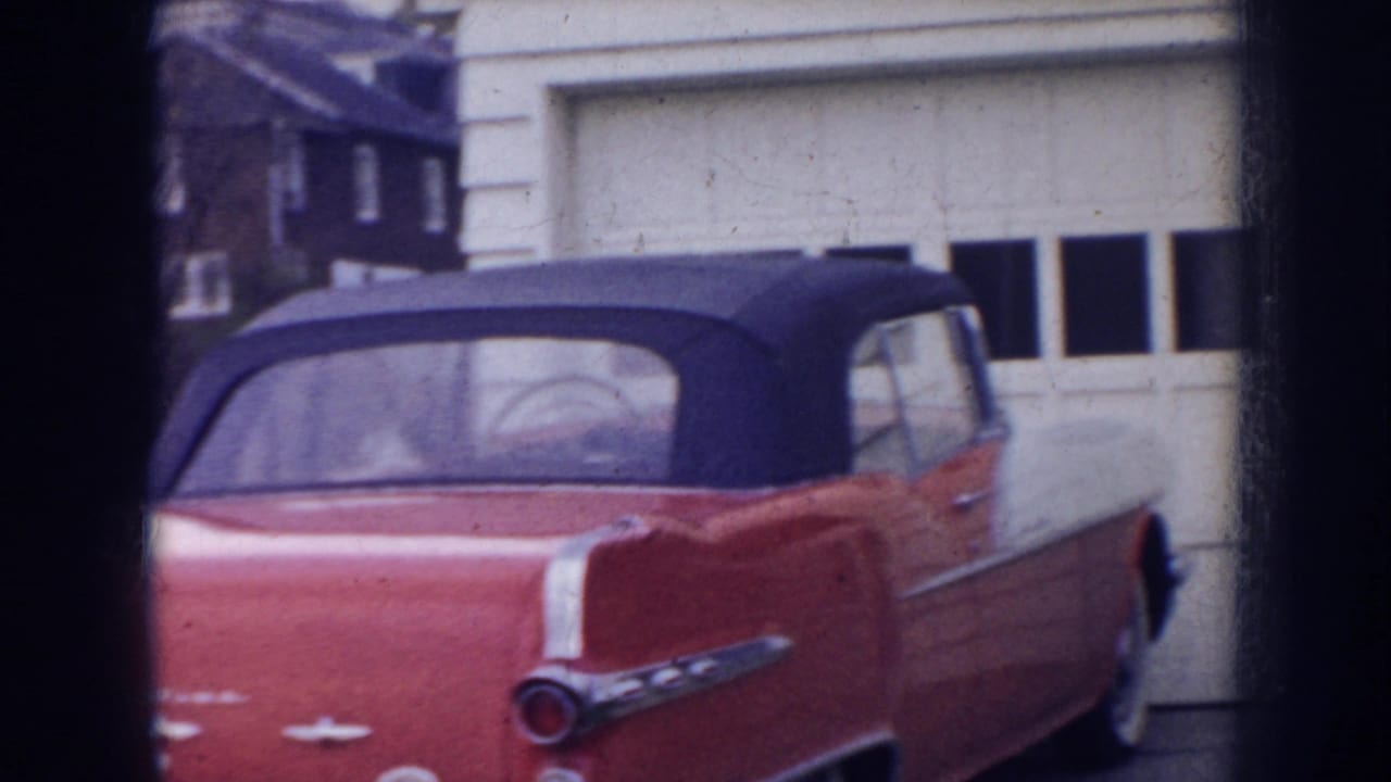 Red convertible parked by a white garage door and house exterior.