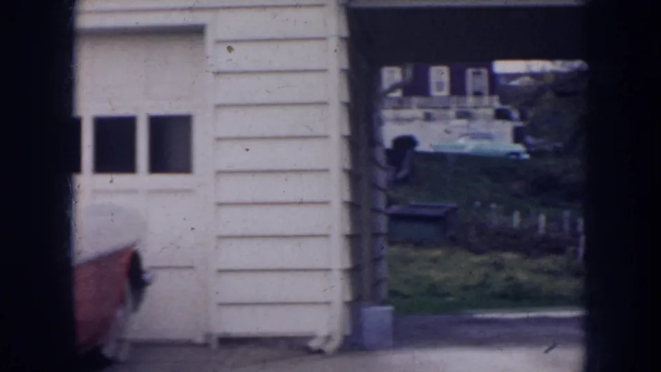 1956 Nebraska home-movie frame showing part of the red convertible near a garage opening and driveway entrance.