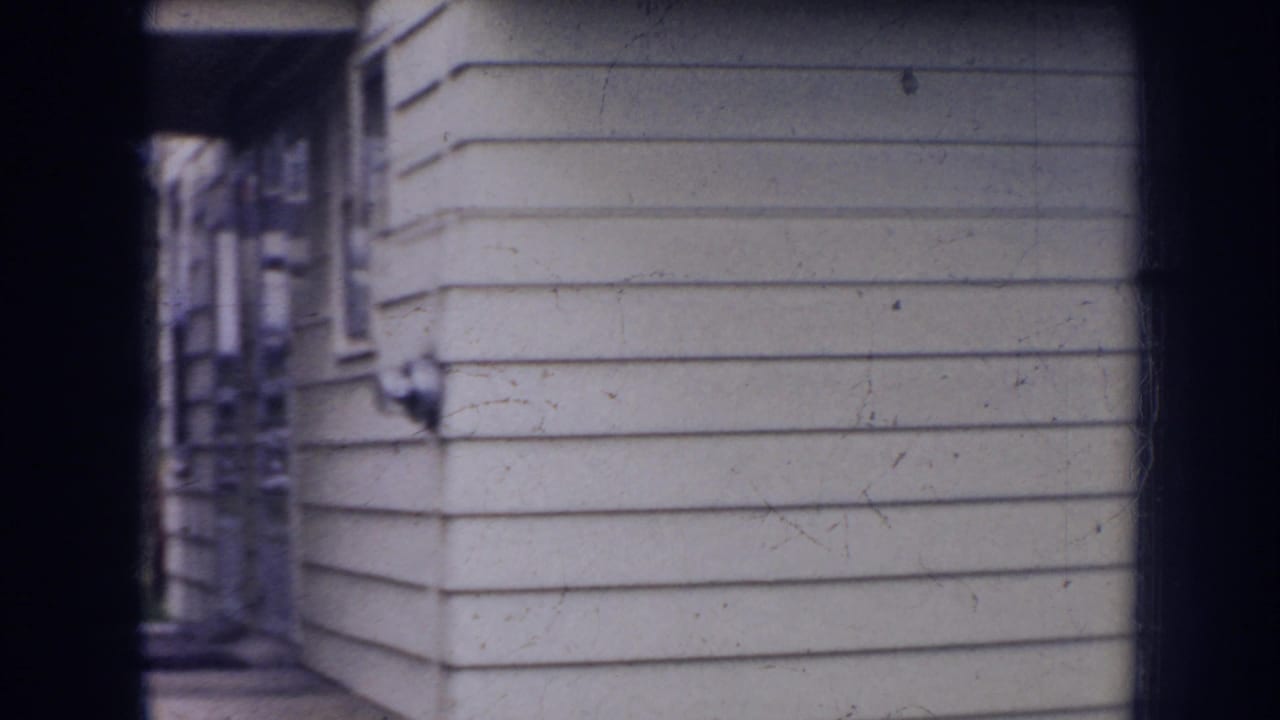 1956 Nebraska 8mm frame showing the side of a light-sided house with a narrow walkway and soft home-movie focus.