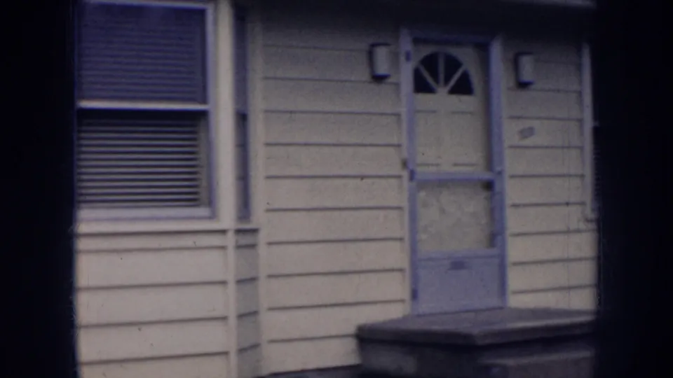 1956 Nebraska home exterior showing a front door, porch steps, window blinds, and small wall lights.