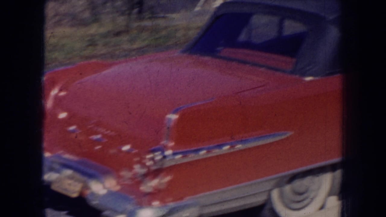 1956 Nebraska 8mm frame showing a red mid-century convertible with dark soft top near a white vintage car on a sunny day.