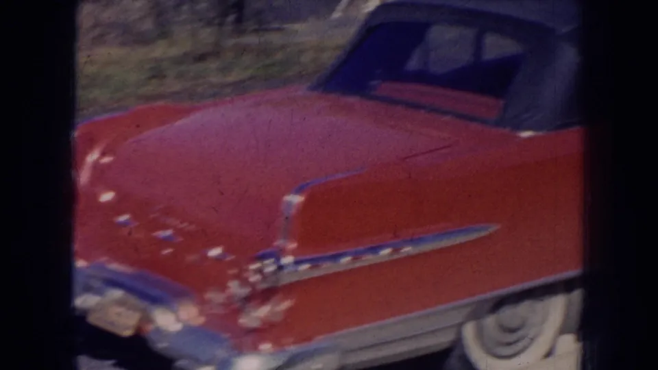 1956 Nebraska 8mm frame showing a red mid-century convertible with dark soft top near a white vintage car on a sunny day.