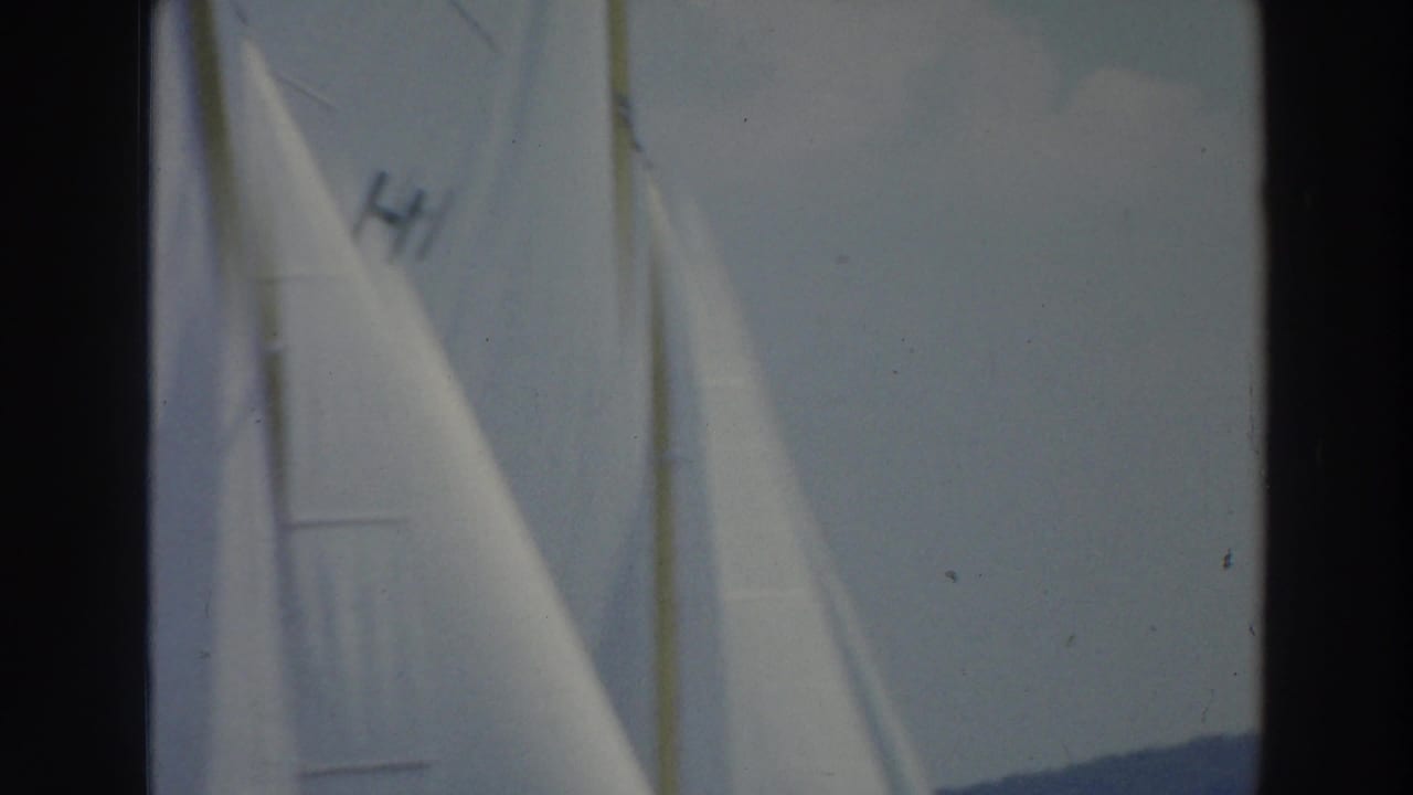 Close 8mm view of white sailboat sails on a Wisconsin lake, including a visible sail marking and distant shoreline.