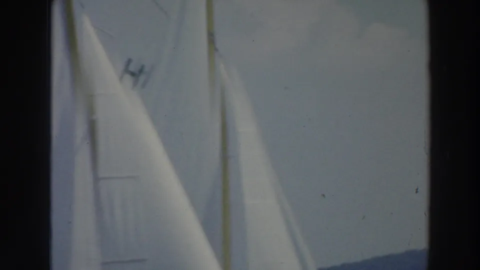 Close 8mm view of white sailboat sails on a Wisconsin lake, including a visible sail marking and distant shoreline.