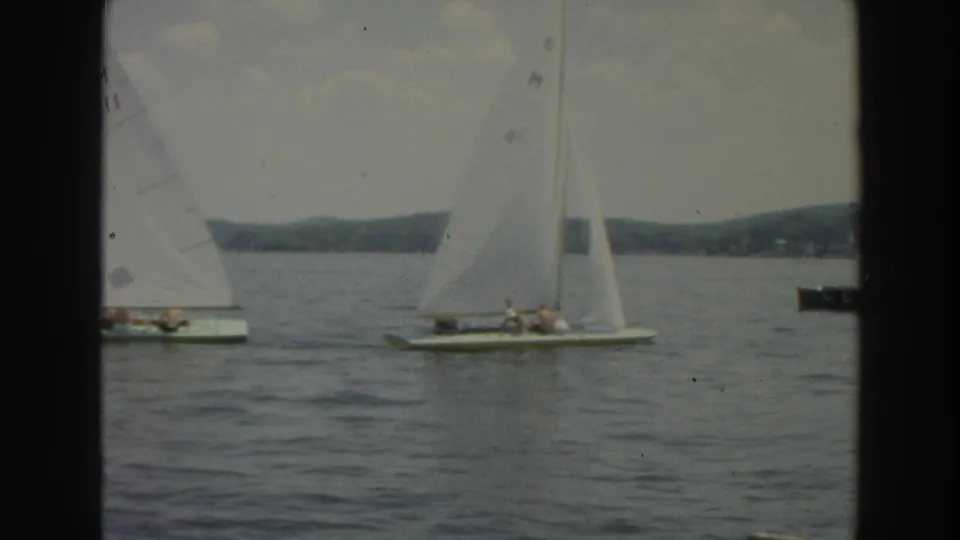 1966 Wisconsin 8mm frame showing small sailboats with white sails on rippled lake water, with a wooded shoreline in the distance.