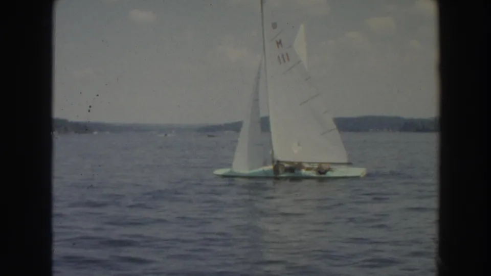 1966 Wisconsin 8mm frame showing a small sailboat with passengers on a lake, framed by soft film grain and distant trees.