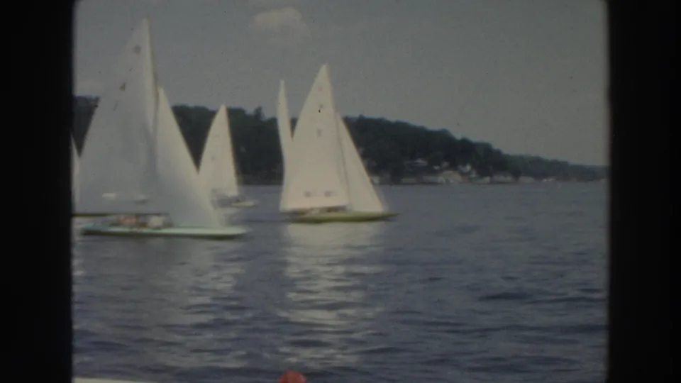 1966 Wisconsin 8mm frame of multiple small sailboats on a lake, with white sails clustered near a tree-lined shore.