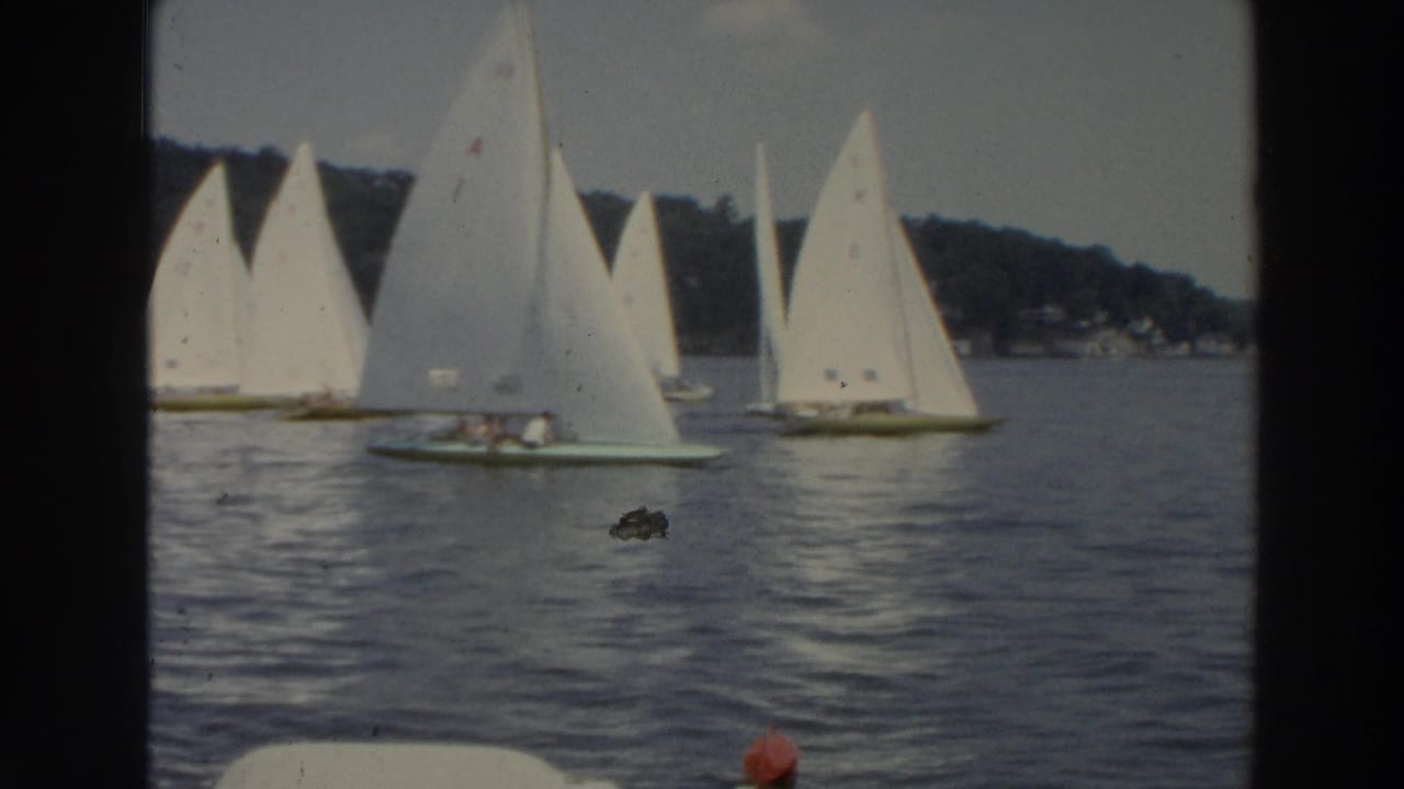 1966 Wisconsin 8mm frame showing small sailboats with white sails on calm lake water near a tree-lined shore.