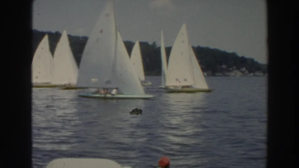 1966 Wisconsin 8mm frame showing small sailboats with white sails on calm lake water near a tree-lined shore.