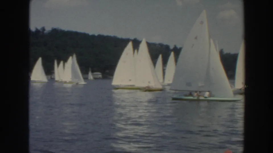 1960s home-movie frame of multiple small sailboats on a Wisconsin lake, with a larger sailboat close to the camera.