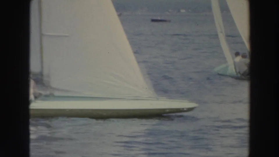 Close 1966 Wisconsin 8mm frame of a white sail and low hull crossing the lake, with another occupied sailboat at the right edge.